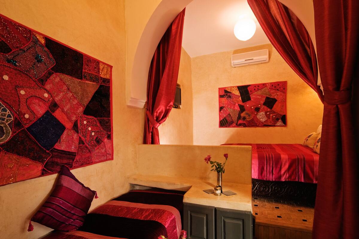 A room with two beds, a small table with a vase, and a wall with a quilt and a painting.
