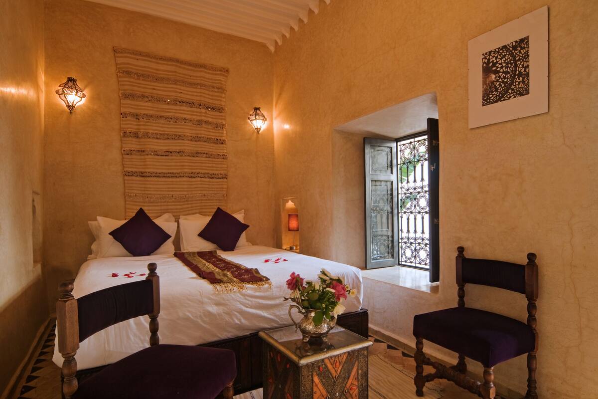 A bedroom with a large bed, two chairs, a nightstand, and a window with a view.