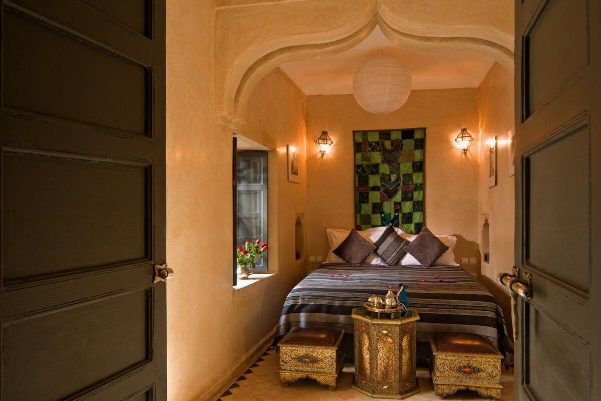 A room with a bed, a small table, and a decorative wall piece.