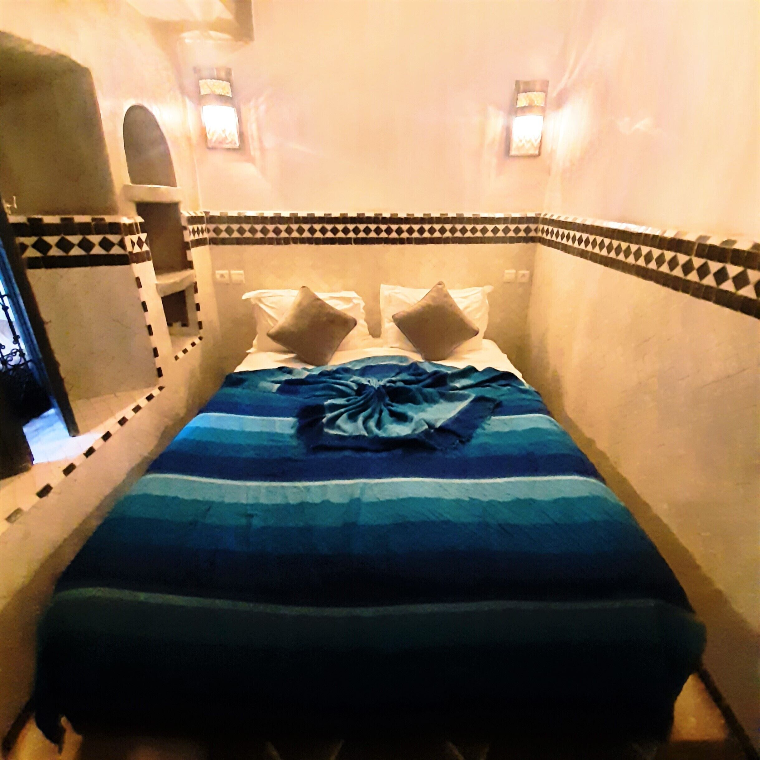 Une petite chambre d’hôtel étroite, avec un lit, deux oreillers et une couverture à rayures.