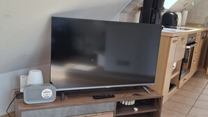 A flat-screen TV on a wooden TV stand with a remote, a speaker, and a small drawer.