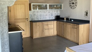 Een keuken met houten kastjes, een betegelde spatwand, een klok en een eethoek met een tafel en stoelen.