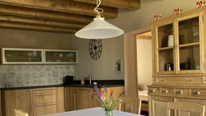 Een eetruimte met een tafel gedekt voor vier personen, houten stoelen, een hanglamp, een klok aan de muur en een houten kast met glazen deuren.