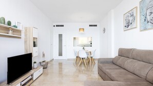 Un soggiorno moderno con una TV a schermo piatto, un divano color beige, un'area pranzo con tavolo e sedie bianche e opere d'arte alle pareti.