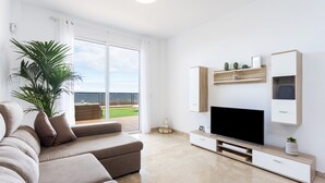 Un soggiorno moderno con una grande TV a schermo piatto, un divano beige e una pianta in vaso.