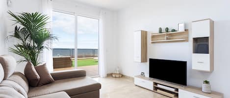 A modern living room with a large flat-screen TV, a beige sofa, and a potted plant.
