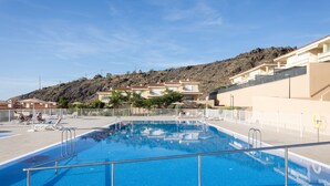 Una piscina con superficie d'acqua cristallina e blu, circondata da una recinzione bianca e un corrimano in metallo. Sullo sfondo, edifici su una collina sotto un cielo sereno.