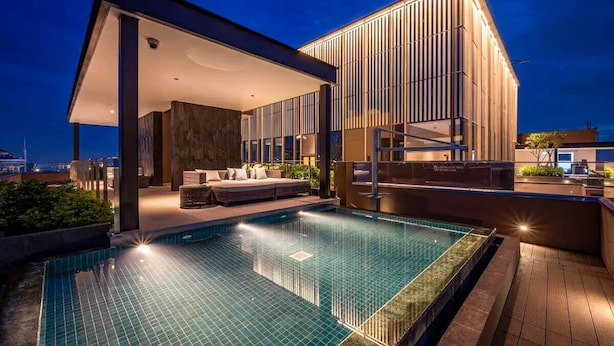 Un hotel moderno con piscina infinita en la azotea, un área de estar exterior techada y un edificio grande de líneas verticales.