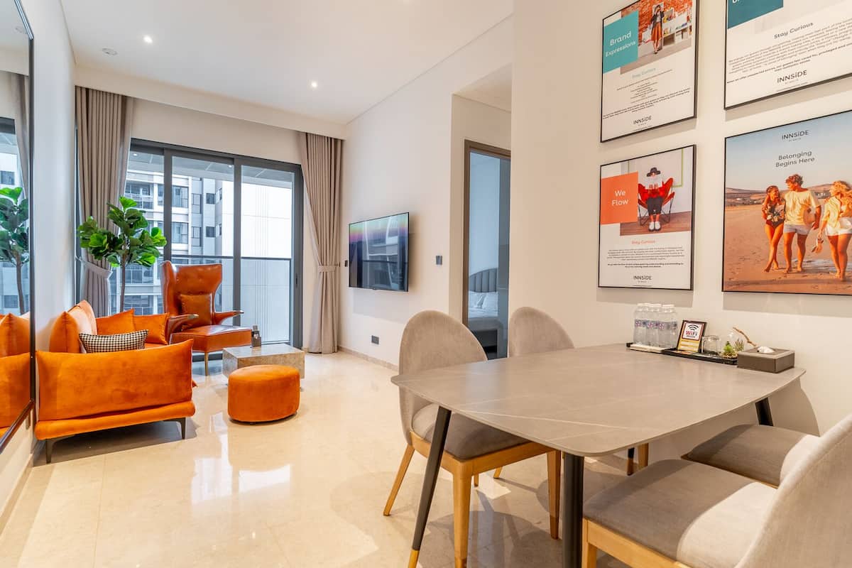 A modern living room with orange sofas, a dining table, and a TV mounted on the wall.