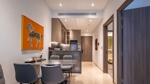 Un comedor moderno con una mesa y sillas, una cocina al fondo y una puerta de madera a la derecha.