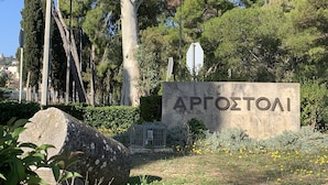 A stone sign with the name "APROZTOAI" in a landscaped area with trees and yellow flowers. - Rouchotas Apartments (Kefalonia)