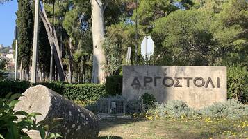 Uma placa de pedra com o nome "APROZTOAI" em uma área arborizada com árvores e flores amarelas.