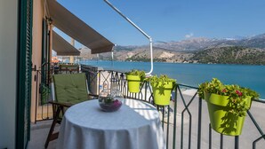 A balcony with a table, chairs, and potted plants overlooking a body of water and mountains. - Rouchotas Apartments (Kefalonia)