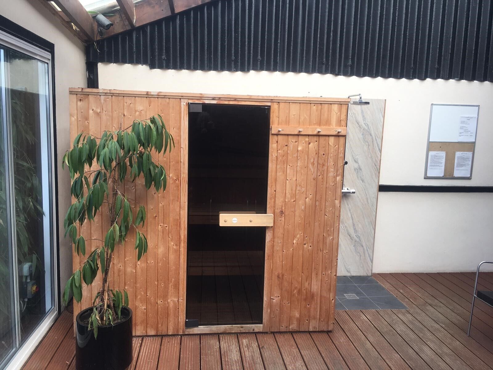 Une structure en bois avec une porte, un pot de fleurs et un sol carrelé.
