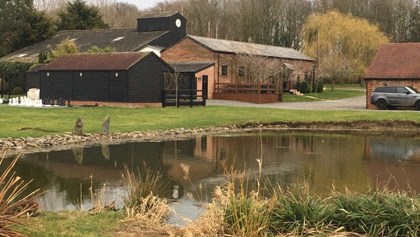 A rustic building with a clock tower, a pond, and a car parked nearby.