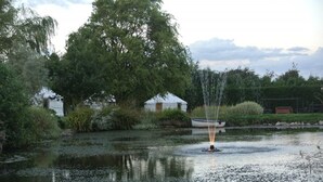 A tranquil pond with a fountain, surrounded by lush greenery and a white gazebo.