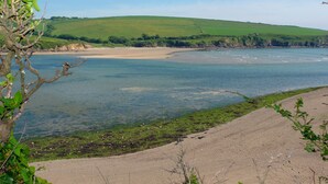 Paesaggio costiero con spiaggia sabbiosa, acque calme e colline verdi sullo sfondo.