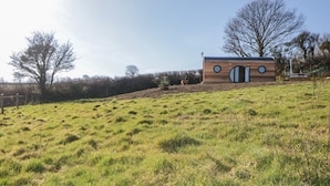 Una casa moderna con un originale design della finestra a forma circolare, situata su una collina erbosa con alberi sullo sfondo.