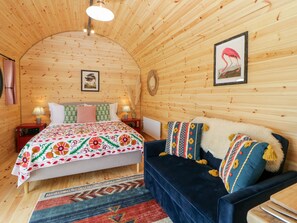 A cozy room with a wooden ceiling, a bed with a floral bedspread, a blue sofa with patterned cushions, and a framed flamingo picture on the wall. - Yealm (Plymouth)