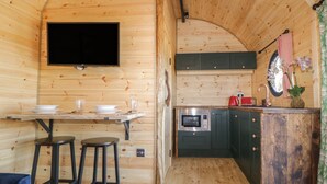 Ambiente in legno con zona pranzo, sgabelli da bar, televisore a schermo piatto, forno a microonde e lavello.