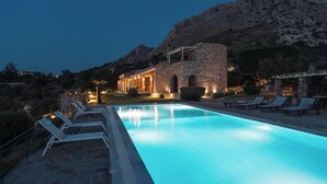 A pool with lounge chairs, a stone building, and a mountain backdrop. - Terra Cassa Private Villa (Aegina)