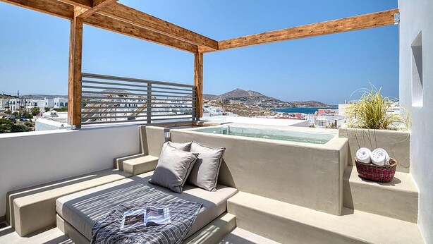 A rooftop terrace with a wooden pergola, a seating area with cushions, and a view of the sea and cityscape. - Clementina Paros (Paros)