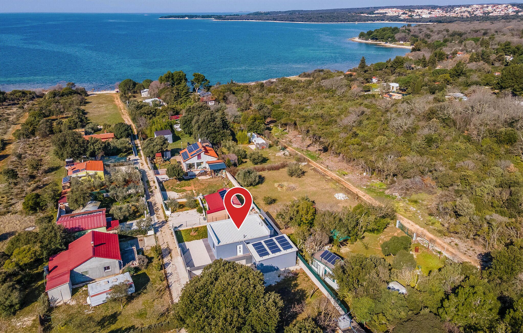 Vue aérienne d’une zone résidentielle côtière, avec des maisons, des panneaux solaires et un emplacement clairement indiqué.