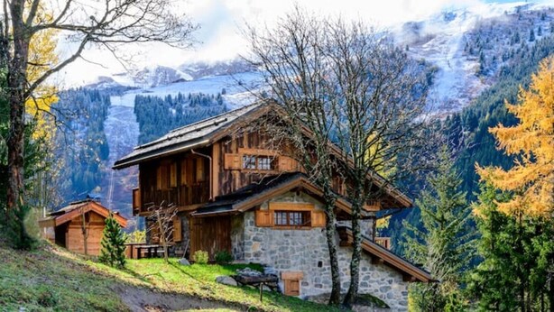 A wooden chalet with stone walls, set in a mountainous area with a view of snow-capped peaks. - Gorgeous, truly ski-in ski-out chalet with hot tub, sauna, fabulous views (Les Allues)