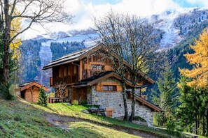 Una baita di legno con pareti in pietra, immersa in un paesaggio montano con vista su cime innevate.