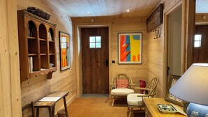 A cozy wooden interior with a bookshelf, two chairs, a table, and a lamp. - Gorgeous, truly ski-in ski-out chalet with hot tub, sauna, fabulous views (Les Allues)