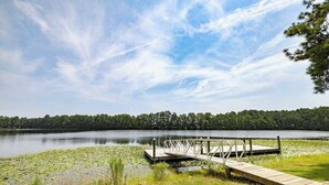 Une jetée en bois s’étendant sur un lac paisible, entouré de verdure et d’arbres.
