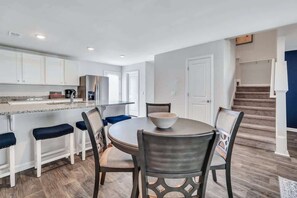 A modern kitchen with white cabinets, a granite countertop, and a dining area with a round table and chairs. - Home Sweet Home w/King Bed (Port Wentworth)
