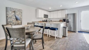 Une cuisine moderne avec des meubles blancs, des appareils en acier inoxydable et un coin repas comprenant une table ronde et des chaises.