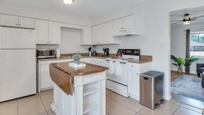 Une cuisine moderne avec des meubles blancs, un îlot central, un four à micro-ondes, une cuisinière et une poubelle.