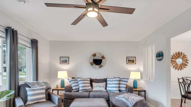 Un salon doté d’un ventilateur de plafond, d’un ensemble de canapés, de deux tables d’appoint avec des lampes et d’un grand tapis.