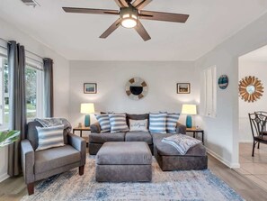 Ein Wohnzimmer mit Deckenventilator, einer Sofagarnitur, zwei Beistelltischen mit Lampen und einem großen Teppich.