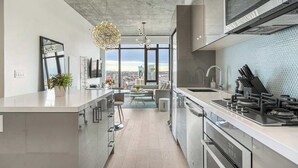 Une cuisine moderne dotée d’un grand îlot central, d’appareils électroménagers en acier inoxydable et offrant une vue sur la ville grâce à de grandes fenêtres.