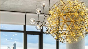 Un salon moderne doté d’une grande fenêtre, d’un lustre aux motifs géométriques et offrant une vue sur le paysage urbain.