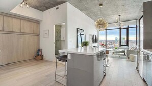 Une cuisine moderne dotée d’un grand îlot central, d’un coin repas offrant une vue agréable et de grandes fenêtres donnant sur le paysage urbain.