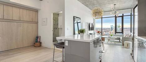 A modern kitchen with a large island, a dining area with a view, and a cityscape visible through large windows.