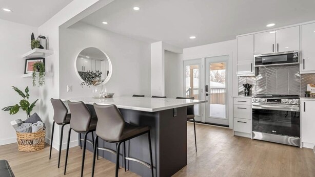 A modern kitchen with a central island, dark chairs, and a large stove. - Welcome to this charming, newly renovated home in the heart of Bowness, one of Calgary’s most beloved and character-filled neighbourhoods. Known for its small-town feel, access to nature, and vibrant local scene, Bowness is the perfect home base. (Calgary)