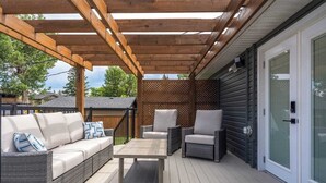 An outdoor patio with a wooden pergola, a wicker sofa with cushions, two armchairs, and a small table. - Welcome to this charming, newly renovated home in the heart of Bowness, one of Calgary’s most beloved and character-filled neighbourhoods. Known for its small-town feel, access to nature, and vibrant local scene, Bowness is the perfect home base. (Calgary)
