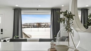 A modern dining area with a marble table, a glass dome centerpiece, and a view of a snowy landscape through large windows. - Welcome to this charming, newly renovated home in the heart of Bowness, one of Calgary’s most beloved and character-filled neighbourhoods. Known for its small-town feel, access to nature, and vibrant local scene, Bowness is the perfect home base. (Calgary)
