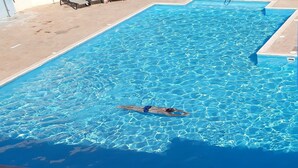 A rectangular swimming pool with clear blue water and a swimmer in the center. - Pissouri stylish and spacious contemporary 2 bedroom apartment (Pissoúri)