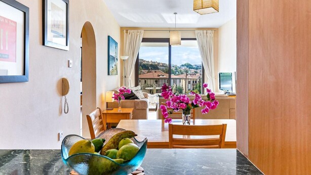 A dining area with a marble table, chairs, and a bowl of fruit. There is a view of a balcony with a cityscape in the background. - Pissouri stylish and spacious contemporary 2 bedroom apartment (Pissoúri)