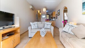 A modern living room with a sofa, a coffee table, a TV, and a kitchen area in the background. - Pissouri stylish and spacious contemporary 2 bedroom apartment (Pissoúri)