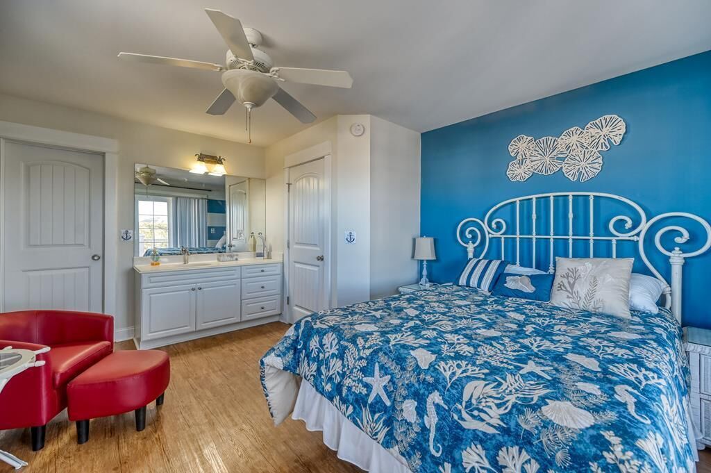 A bedroom with a bed, a ceiling fan, a red chair, a white dresser, and a blue wall.