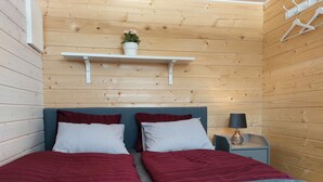 A bedroom with two beds, a nightstand with a lamp, a shelf with a plant, and wooden walls. - Swedish-style guest house in the beautiful nature and tranquillity of central Sweden. (Stöde)