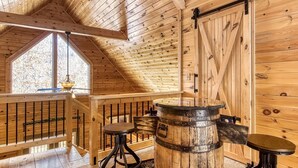 Interior de madera con techo inclinado, un barril grande y una puerta corredera de granero.