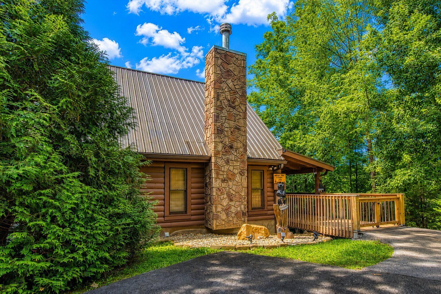 A log cabin with a stone chimney, a covered porch, and a wooden deck.